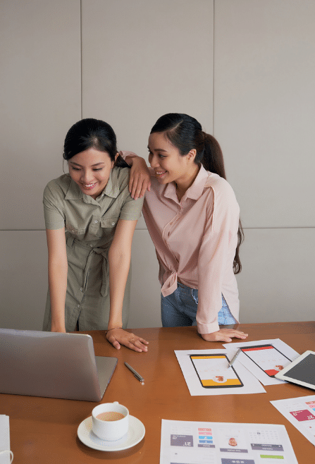 Two Friendly Female Colleagues Standing Desk work Looking Laptop Screen